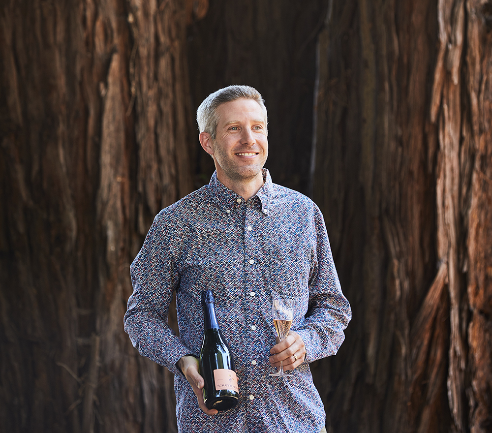 Winemaker Jeffrey Jindra holding a bottle and glass of sparkling wine.