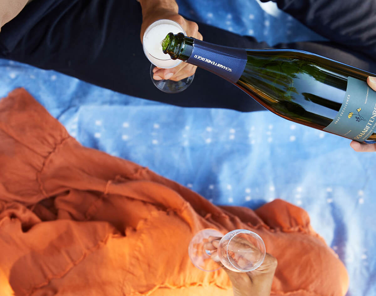 Share Club, pouring sparkling wine on a picnic blanket.